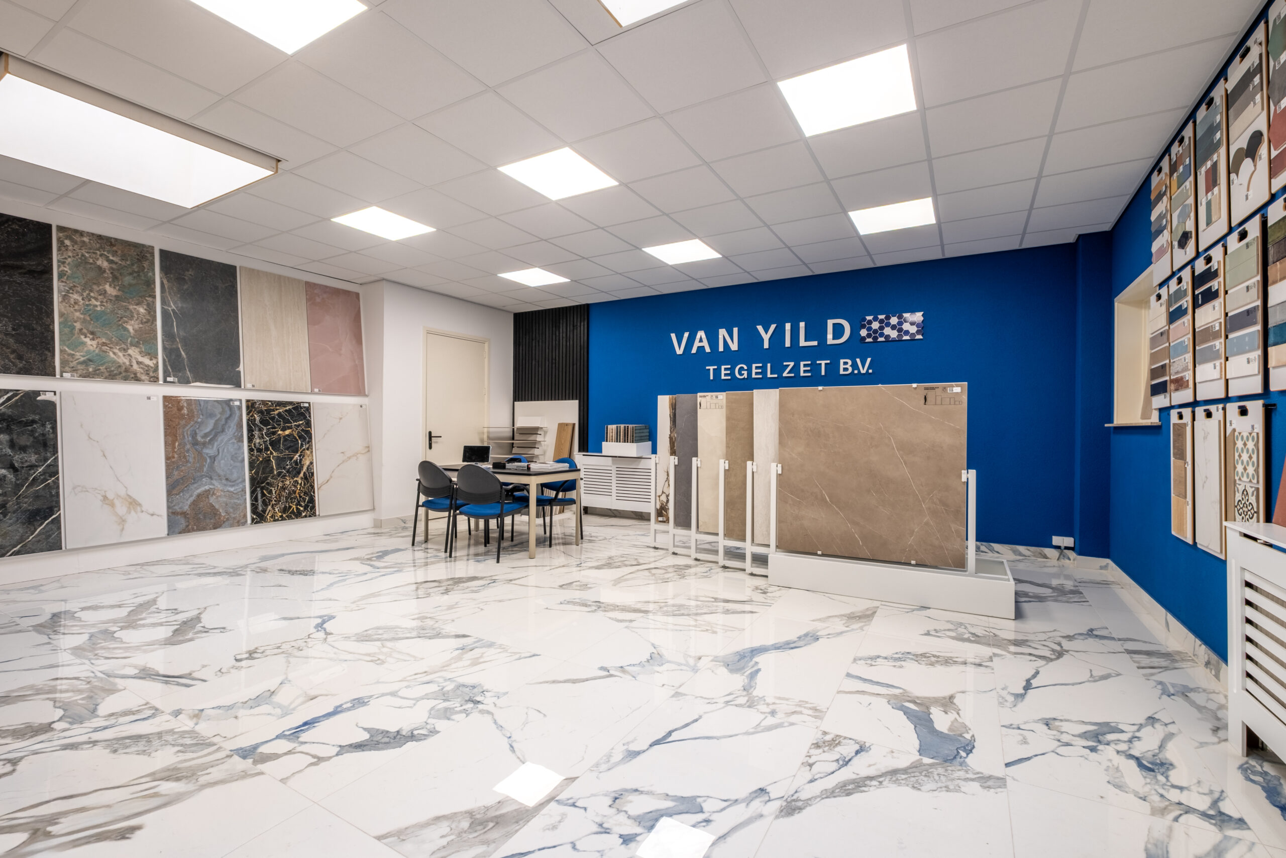 De showroom van Van Yild Tegels met tegelpanelen langs de wanden en een marmerlook vloer